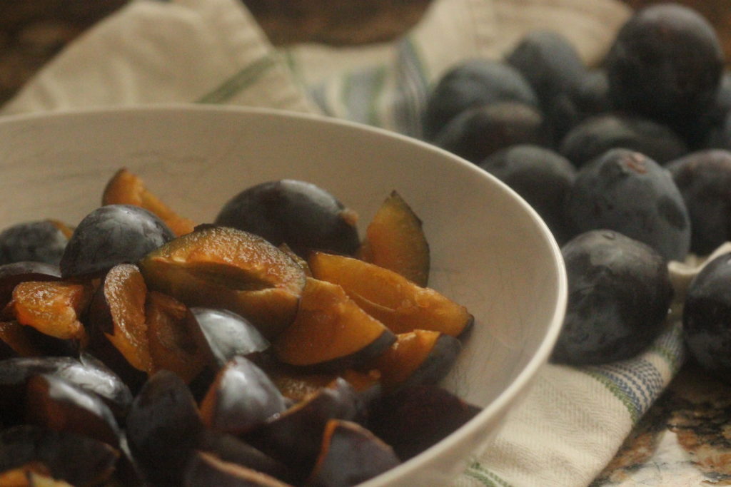 italian plums cut into quarters in a white bowl
