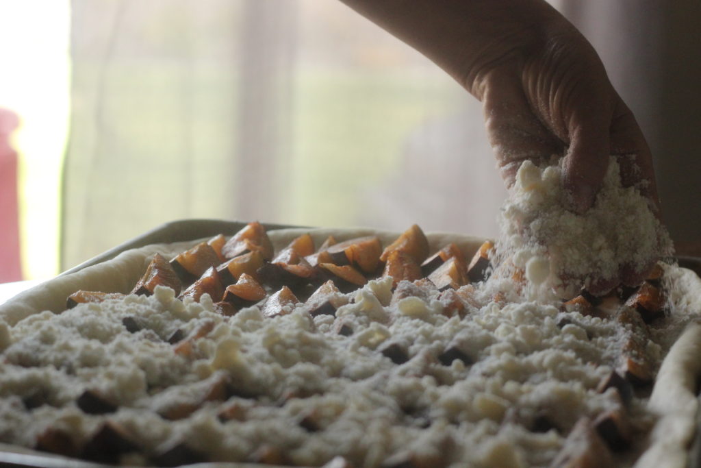 sprinkling crumb mixture over a pan of plum cake