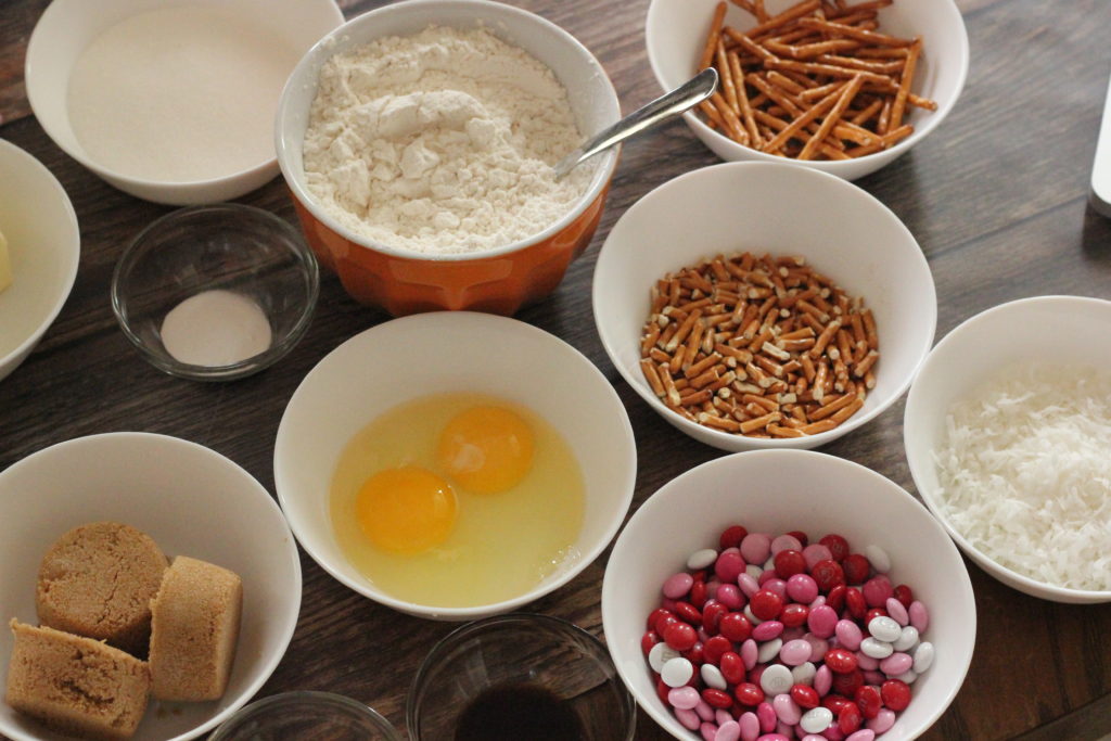 Ingredients for Coconut Chocolate Crunch Cookies. Picture of eggs, butter, flour, sugars, candies, pretzels and coconut.