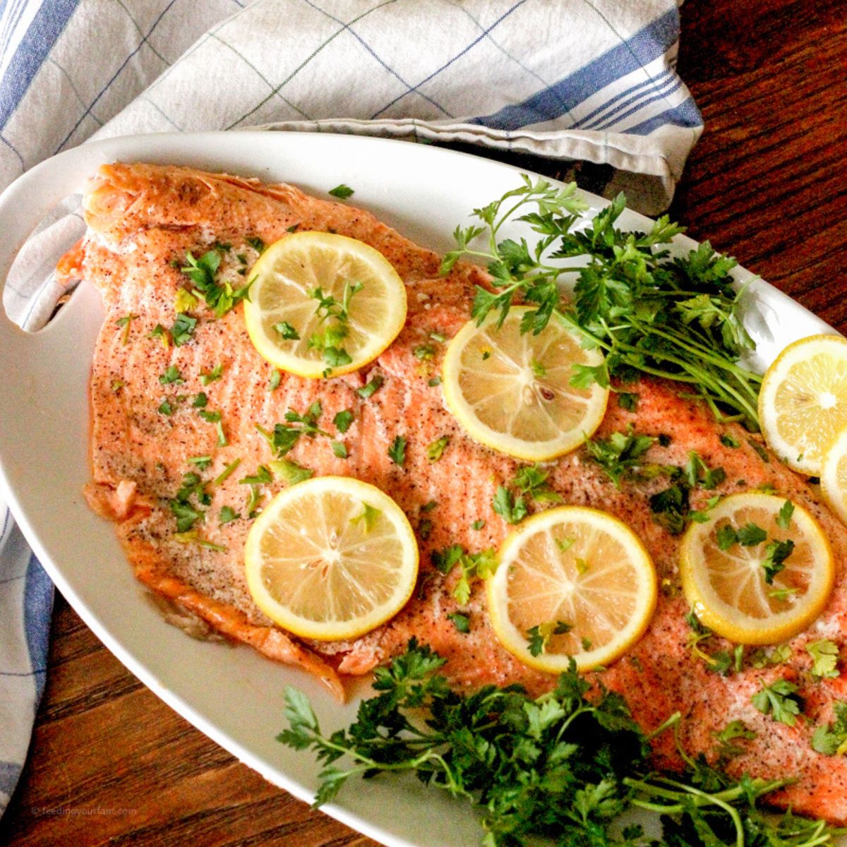 baked salmon topped with lemon slices on a white serving platter