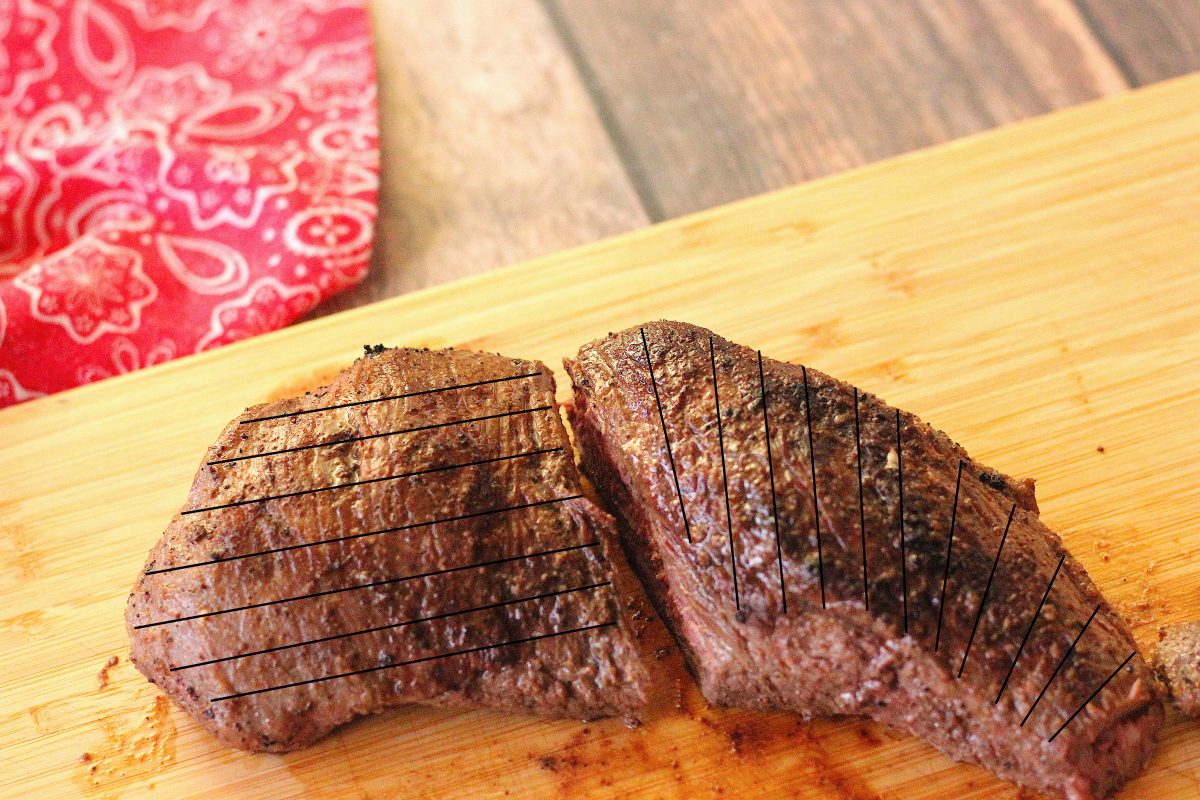 lines on a tri tip roast showing how to slice it against the grain. The tri tip is cut in half on a wooden cutting board.