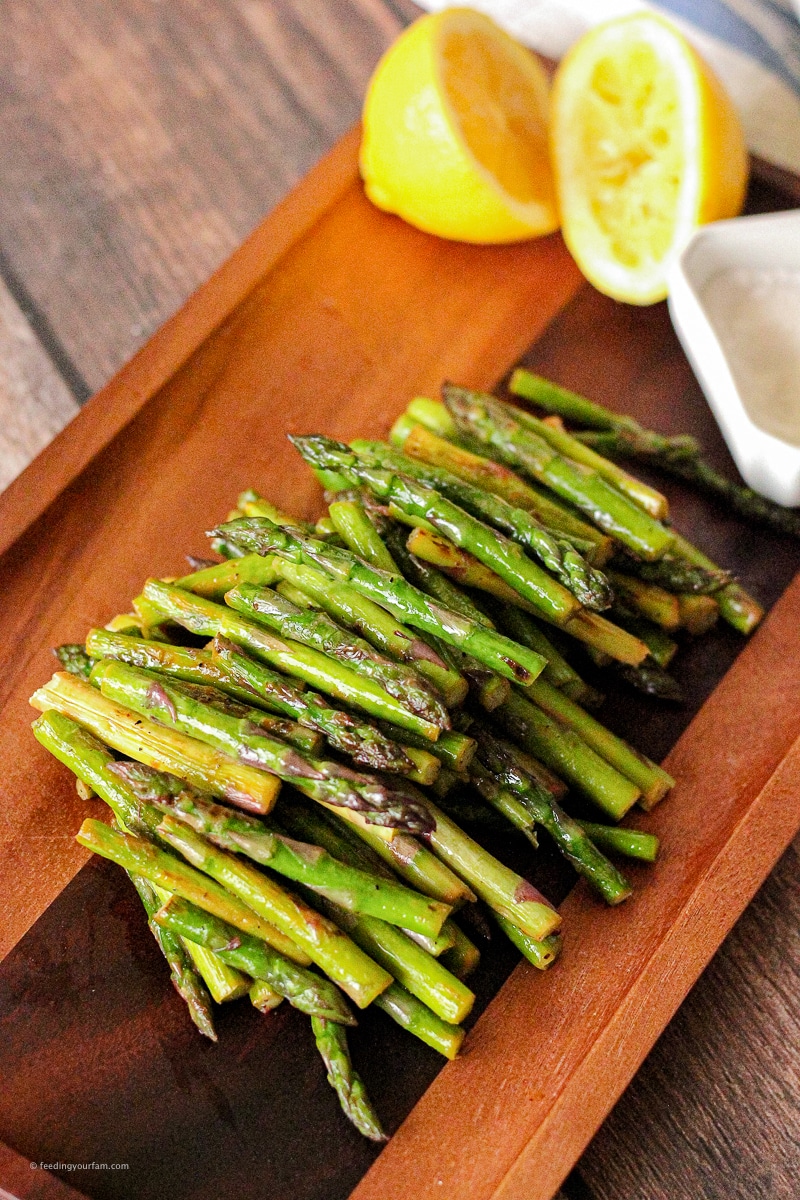 Sauteed Asparagus with Lemon is a quick and delicious side dish that goes perfectly with whatever you are serving! #asparagus #lemonasparagus #lemon #feedingyourfam small stems of asparagus piled on a wooden platter with a side of lemon