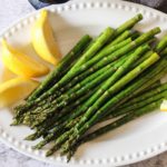 grilled asparagus on a white plate with lemon wedges
