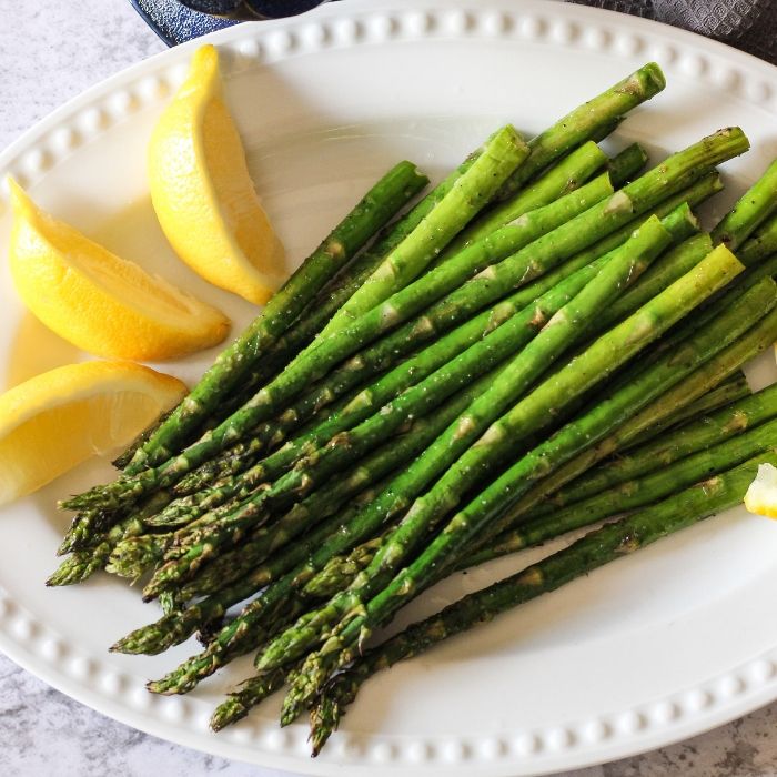 grilled asparagus on a white plate with lemon wedges