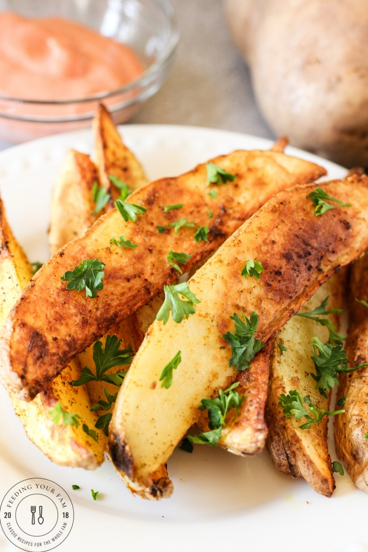 Air Fryer Potato Wedges are seasoned perfectly and cooked to a golden crisp in the air fryer. Served with a tangy greek yogurt dipping sauce, they are the perfect dish to serve as a side dish or tasty mid-day snack! potato wedges//air fryer recipes// air fried potatoes #airfryer #airfriedpotato #potatowedges golden potato wedges on a plate topped with parsley