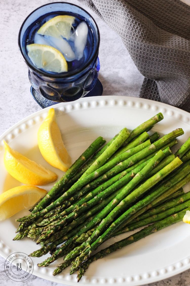 Grilled Asparagus is a special treat and perfect vegetable side dish to whatever you are grilling! This grilled asparagus recipe has a hint of lemon and garlic and couldn't be easier to prep and make! #grilledasparagus #asparagus #asparagusrecipes Grilled asparagus on a white plate with lemon wedges