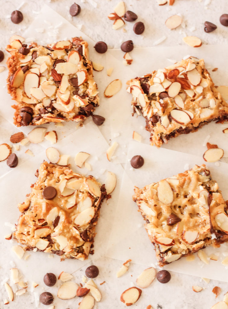 Magic Cookie Bars are layers of delicious graham cracker crust, covered with a gooey caramely layer stuffed with chocolate, nuts, and coconut. These Magic Cookie Bars are perfect to bring to parties, picnics, or just a simple dessert. #cookiebars #cookierecipes #magiccookies magic cookie bars on a white background