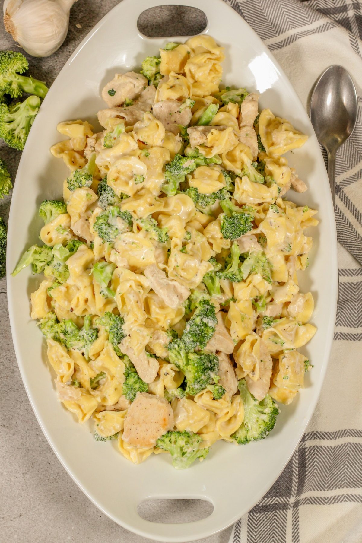 tortellini in a creamy white sauce with broccoli and chicken on a white platter