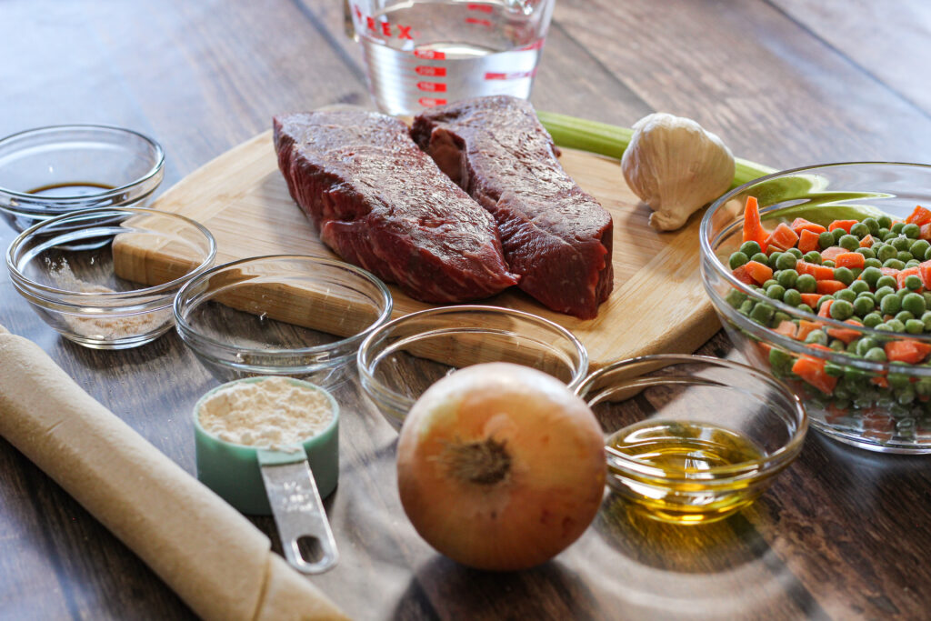 ingredients for beef pot pie. pie crust, steak. onion, garlic, vegetables and spices