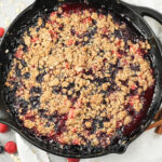 triple berry crisp with cooked berries topped with an oatmeal crips topping in cast iron pan