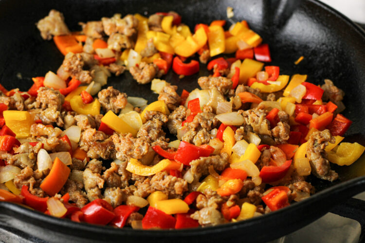 browned sausage, peppers and onions in a black cast iron pan