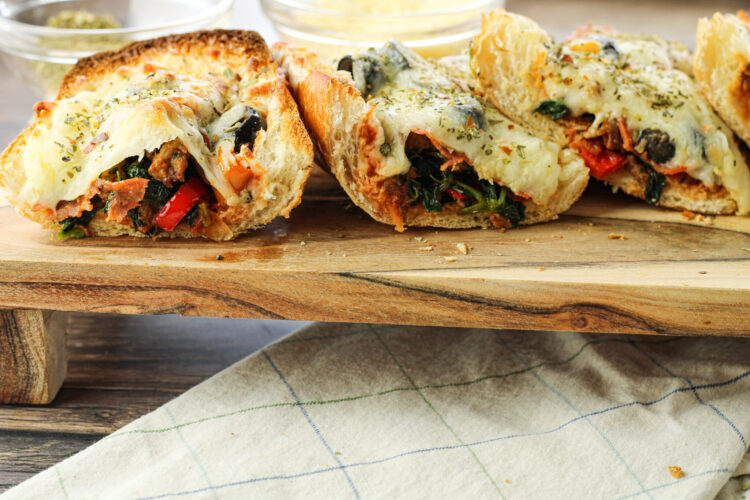 sliced french bread stuffed with pizza toppings, topped with melted cheese on a wooden platter