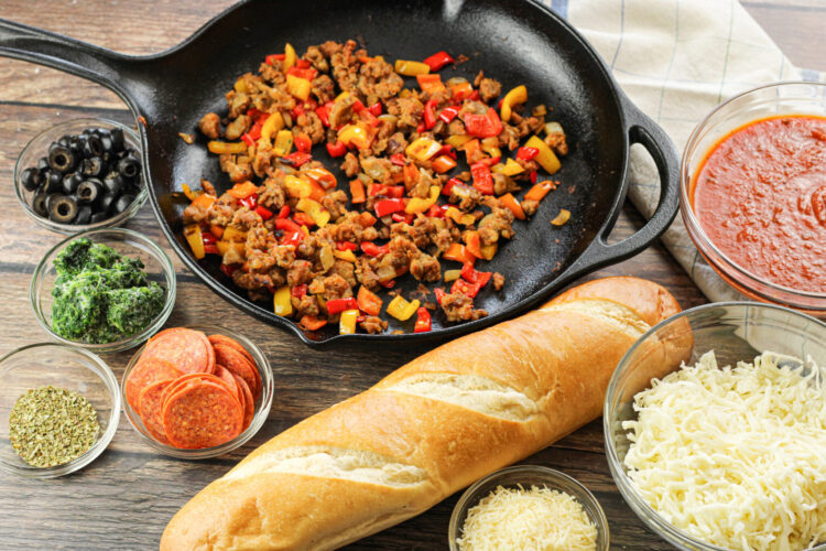 ingredients for french bread pizza. Loaf of french bread, shredded cheese, spaghetti sauce, pepperonis, sausage, spinach olives and oregano