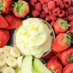 bananas, strawberries, raspberries and green apples surrounding yellow lemon fruit dip in the center