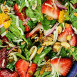 spinach, sliced strawberries, mandarin oranges, mozzarella cheese and toasted almonds in a blue salad bowl
