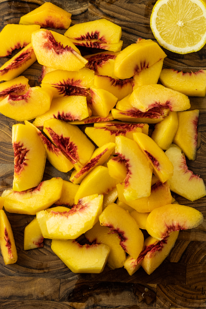 sliced peaches on a wooden cutting board with a half a lemon