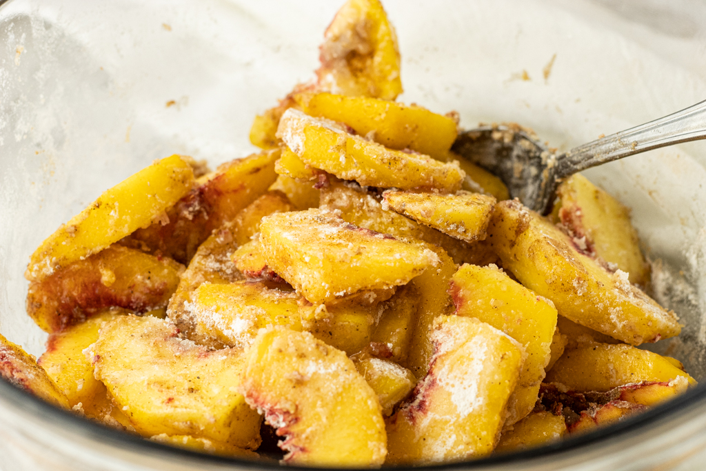 peaches covered in flour, sugar and spices in a mixing bowl
