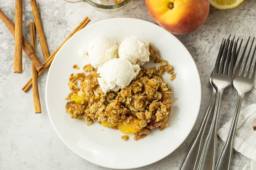 white plate with peach crisp and vanilla ice cream on a white plate
