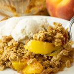 fork lifting a scoop of peach crisp off a white plate