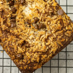 banana bread topped with coconut and chocolate chips on a cooling rack