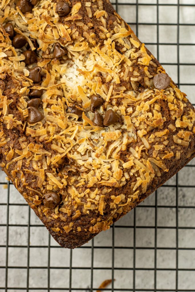 banana bread topped with coconut and chocolate chips on a cooling rack