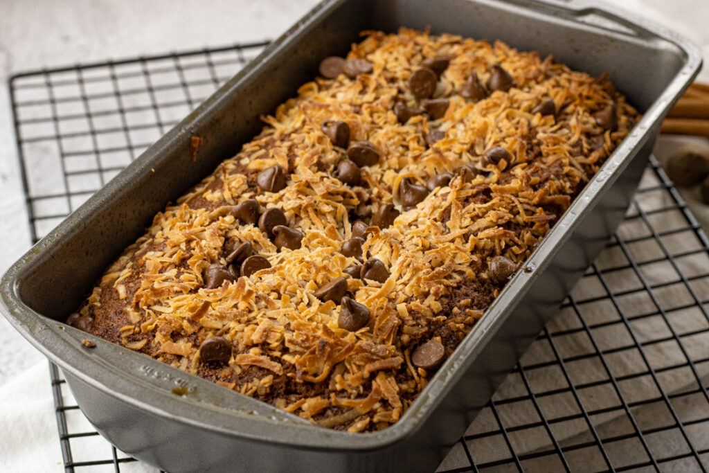 coconut and chocolate covered banana bread in a metal bread ban on a cooling rack