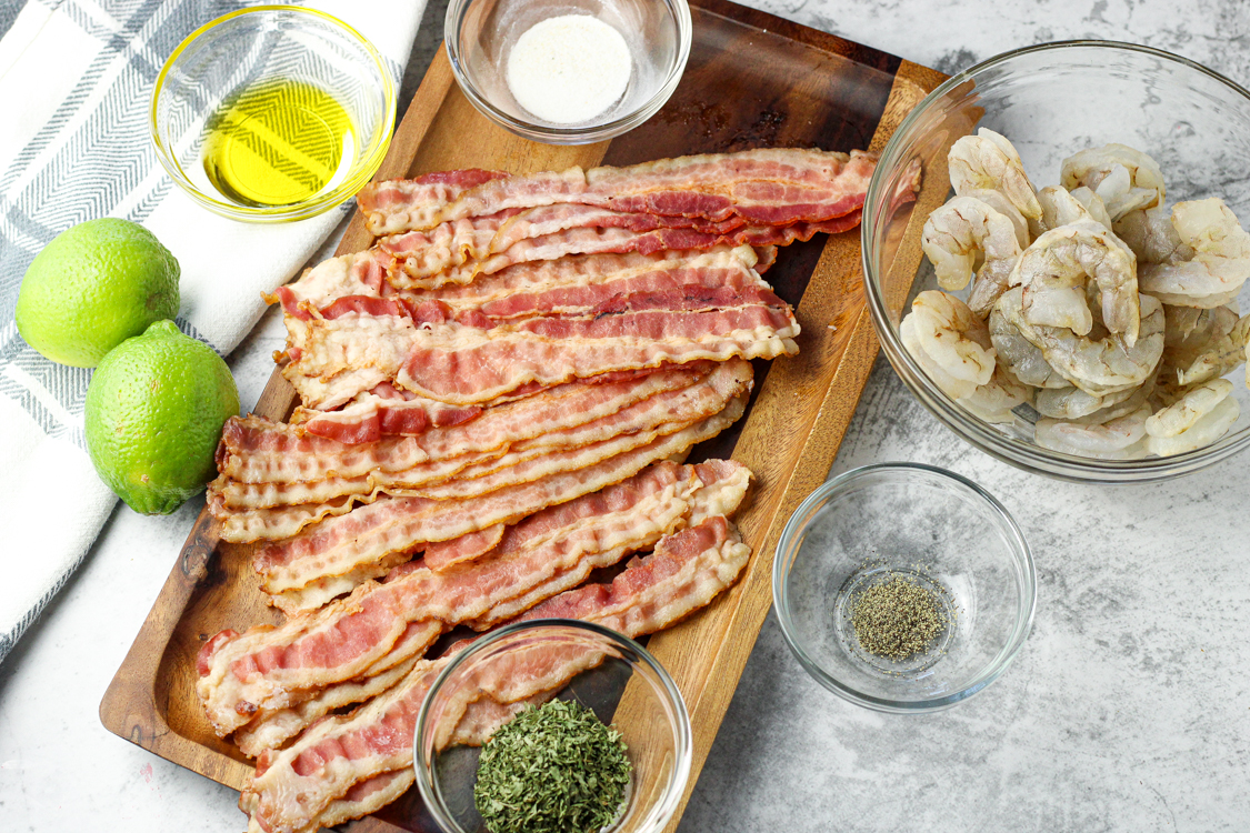 ingredients for bacon wrapped shrimp, bacon, parsley, garlic salt, olive oil, pepper, uncooked shrimp and limes