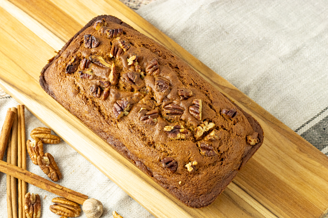 pumpkin bread topped with pecans on a wooden cutting board