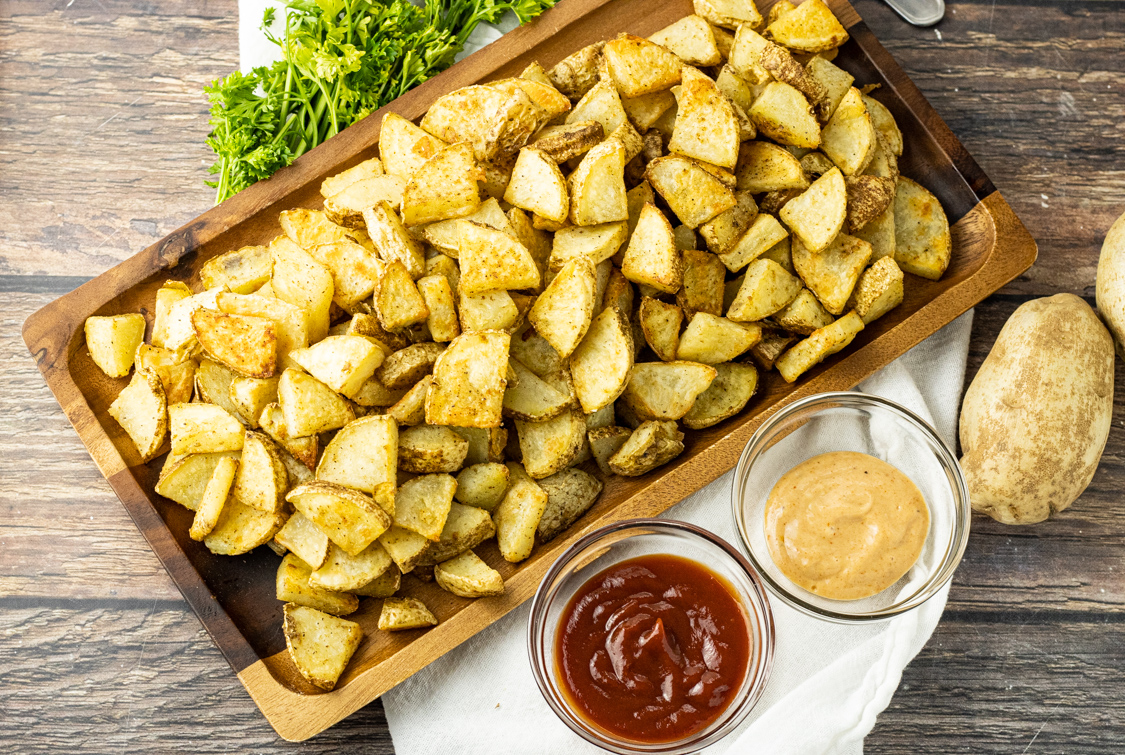 potato triangle pieces on a wooden platter with ketchup and dipping sauce
