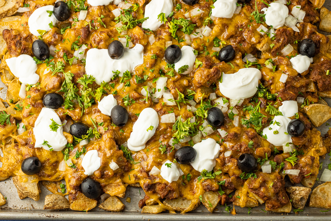 baked potato pieces topped with chili, cheese, sour cream and olives