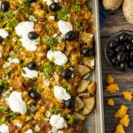 baking sheet of potato pieces topped with chili, sour cream and olives