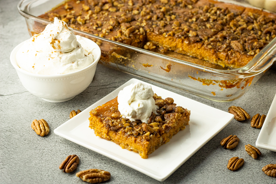 pumpkin pie slice on a white plate topped with whipped cream