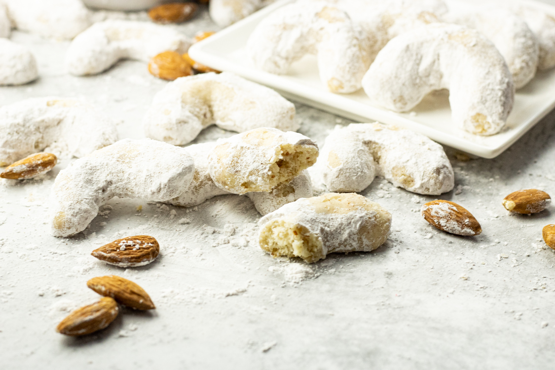 powder sugar coated almond cookies, with one broken in half to show texture