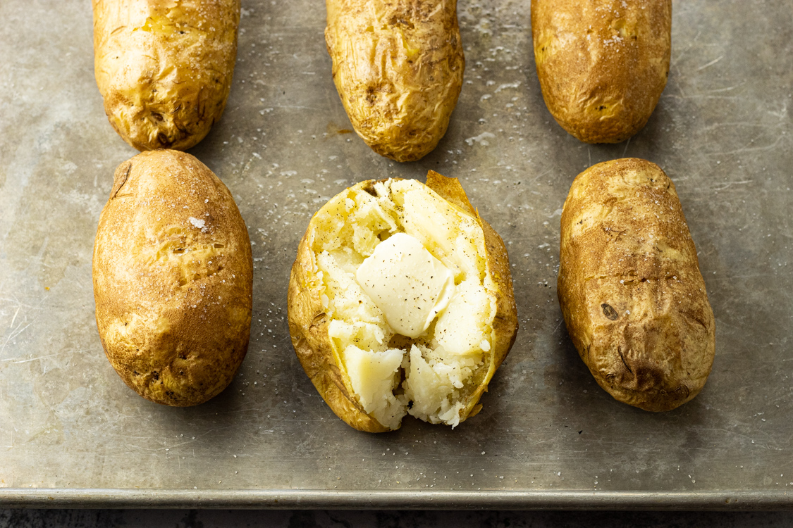 baked russet potatoes on a baking sheet with one split open with butter