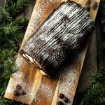 chocolate yule log cake on a wooden platter surrounded by evergreen pines