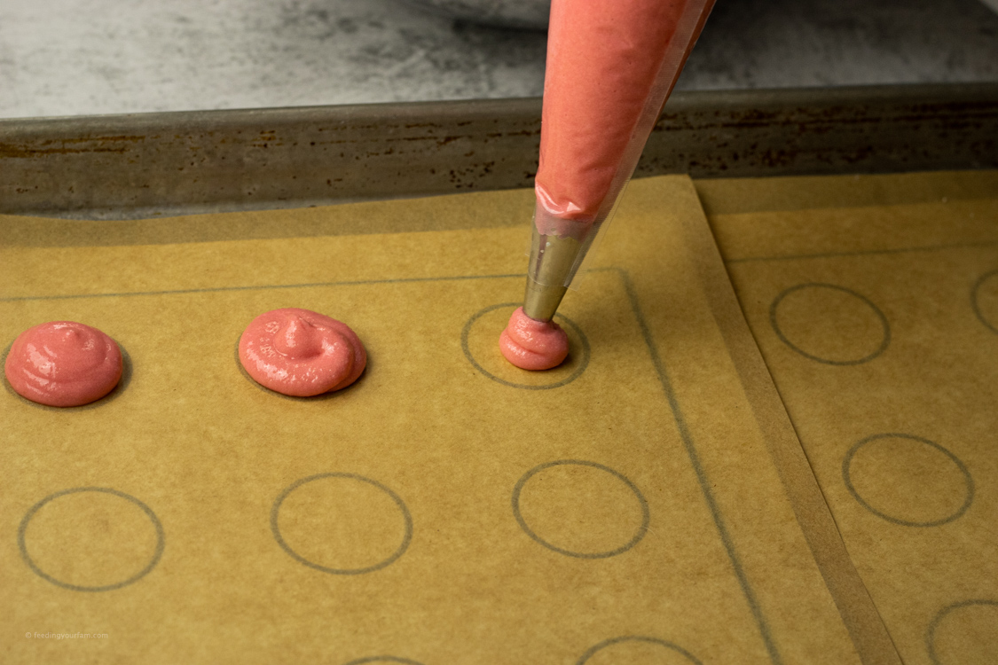 piping pink cookies onto parchment paper lined baking sheet
