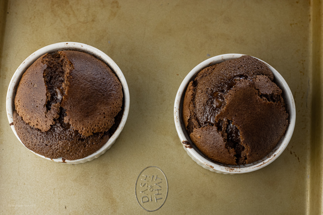2 chocolate cakes in white ramekins on a baking sheet
