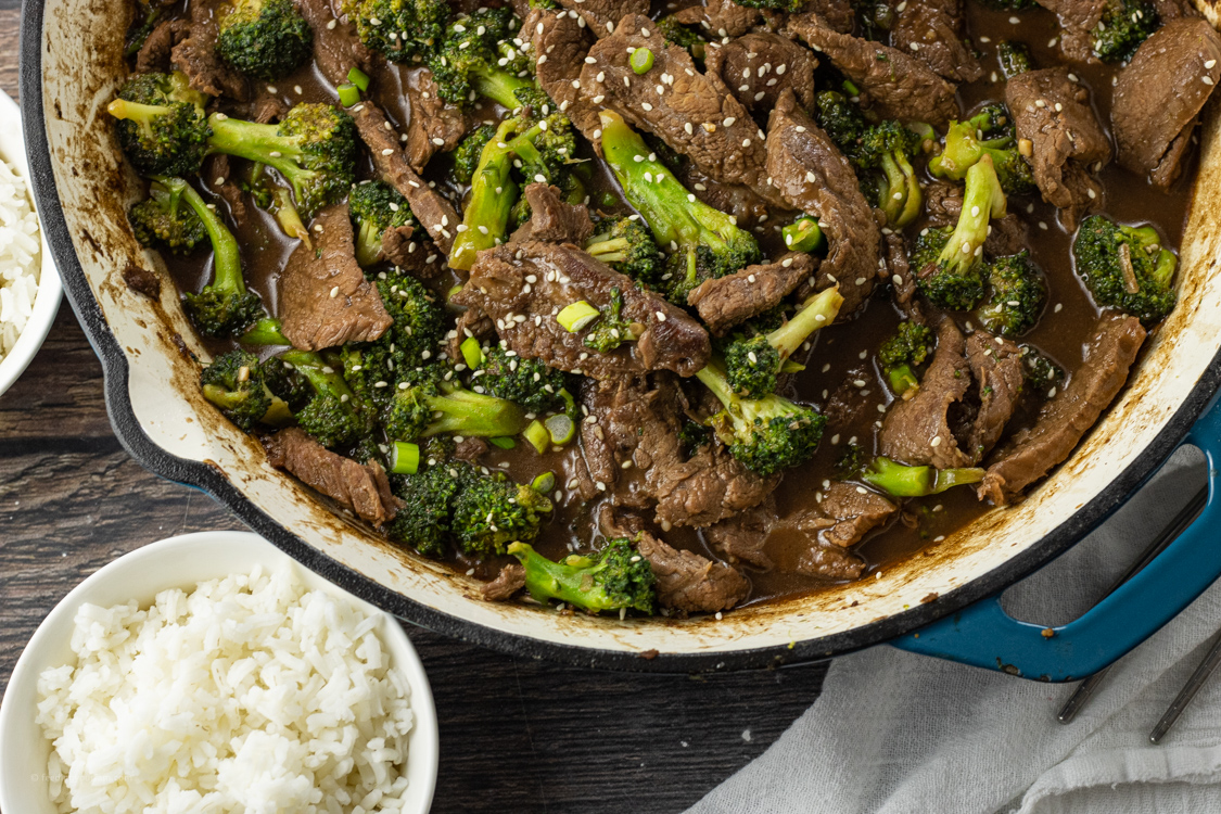 cooked broccoli beef in a pan next to a bowl of white rice