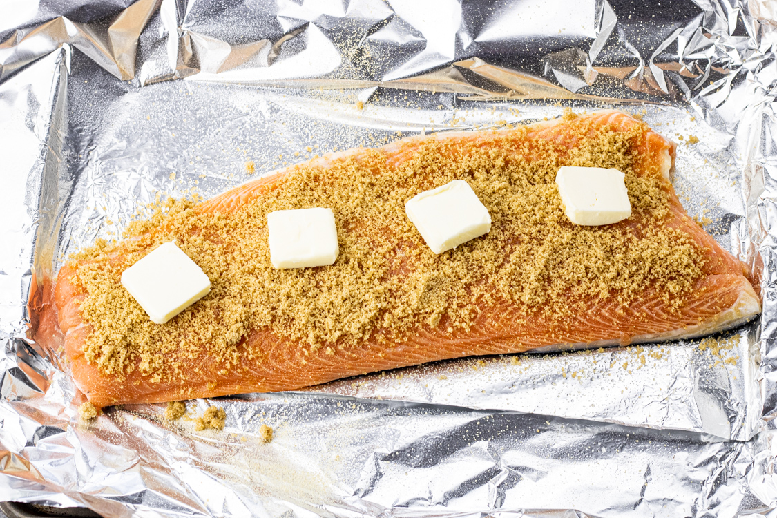 salmon filet on a piece of foil, topped with brown sugar and butter slices