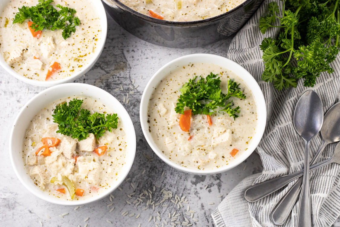 3 bowls of creamy chicken soup with rice topped with fresh parsley