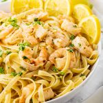 big white bowl of fettuccine noodles and shrimp with lemons