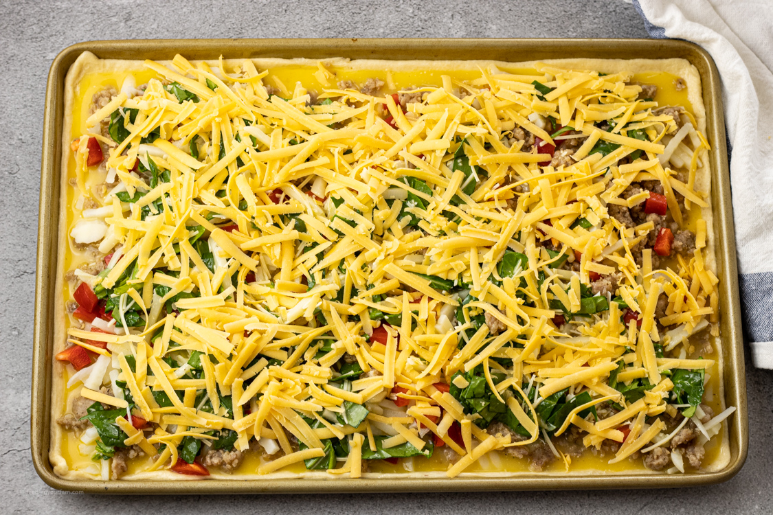 pizza for breakfast topped with sausage, eggs, hash browns and cheese ready to be baked