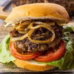 hamburger cooked in cast iron skillet with fried onions, tomato and lettuce on a bun