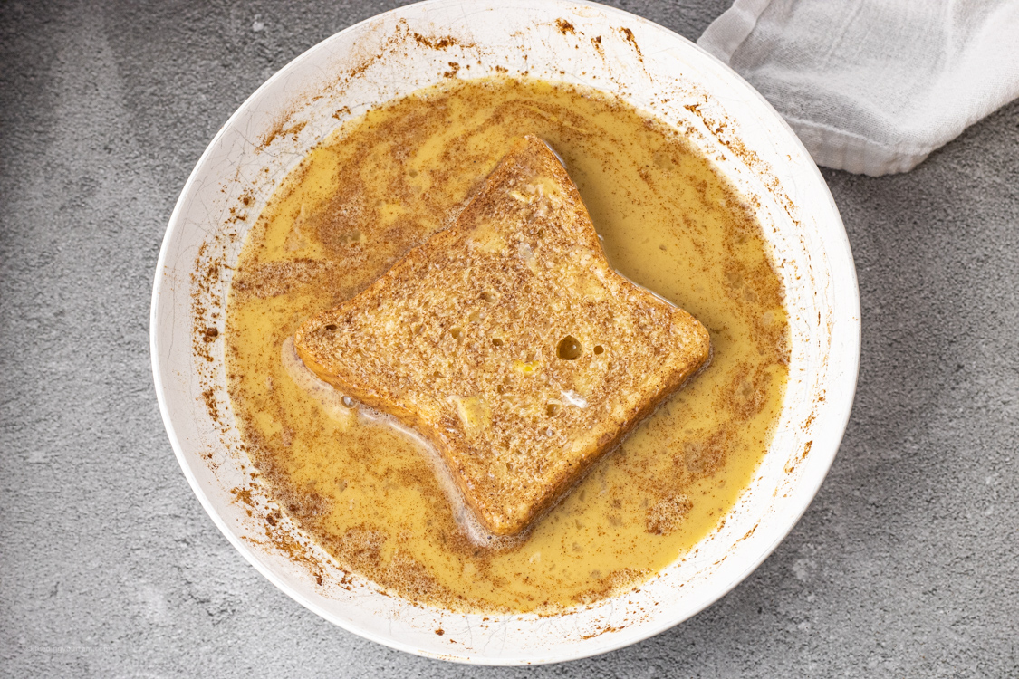 dipping bread in egg mixture in a white bowl