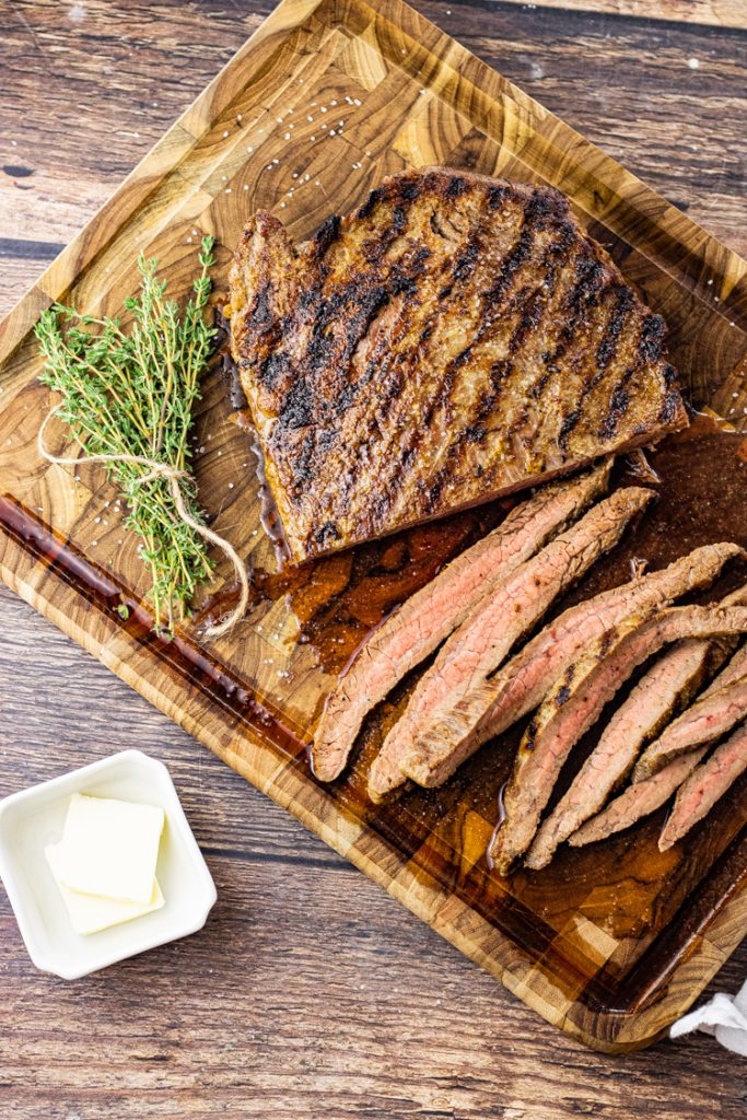 sliced cast iron cooked flank steak on a wooden cutting board
