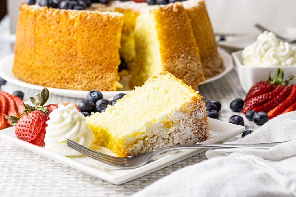 slice of chiffon cake on a white plate with whipped cream, strawberries and blueberries