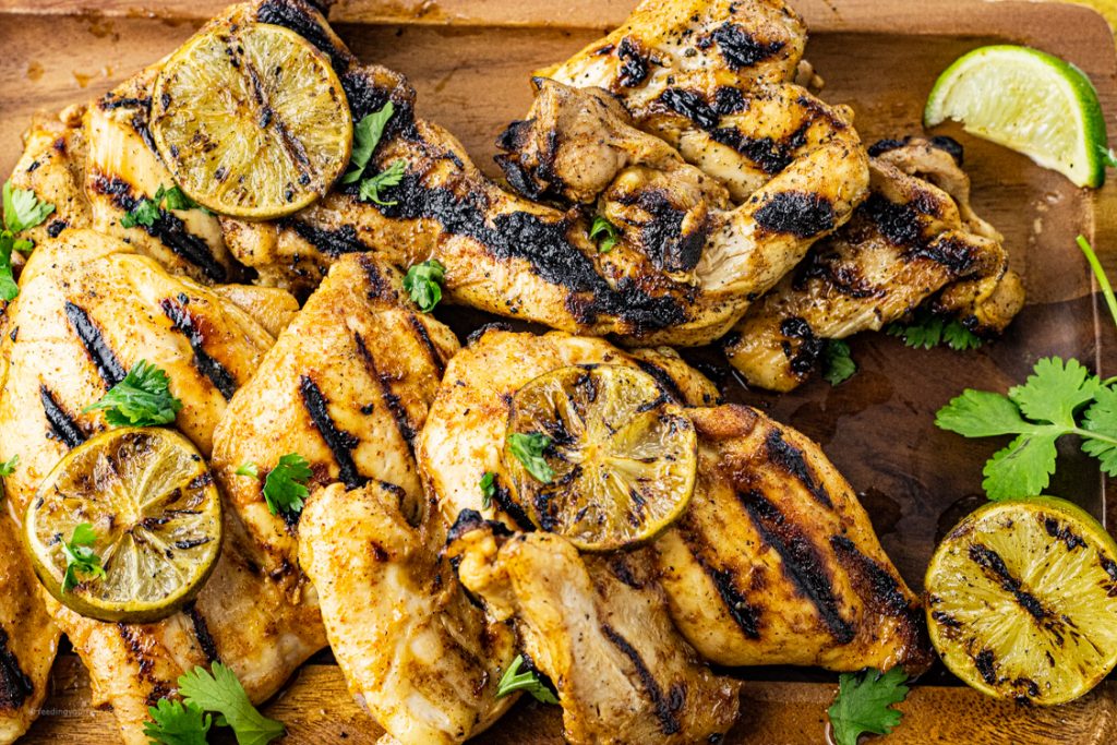 grilled chicken thighs on a wooden serving platter topped with lime slices. 