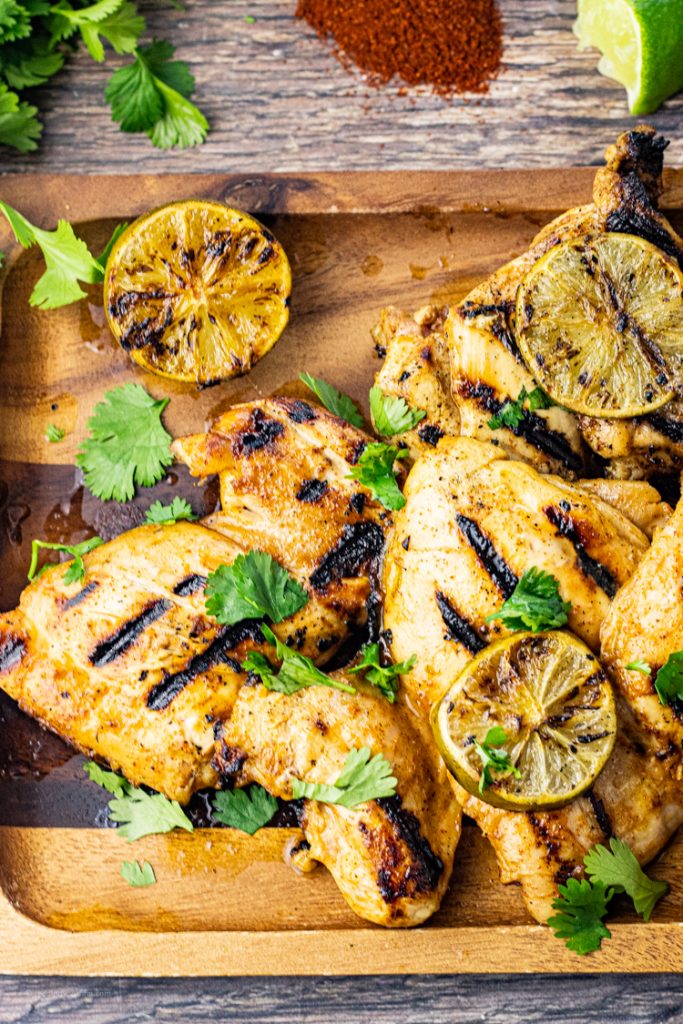 pieces of grilled chicken thighd on a wooden platter