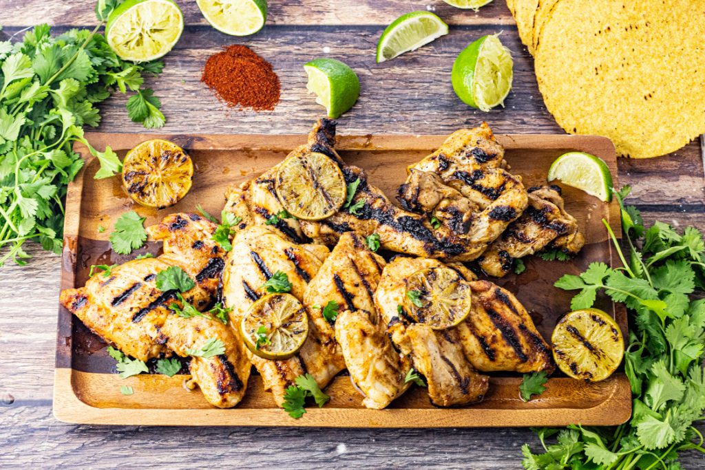 grilled chicken on a wooden serving platter with slices of lime