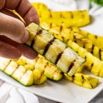 a hand holding a piece of zucchini that has been grilled